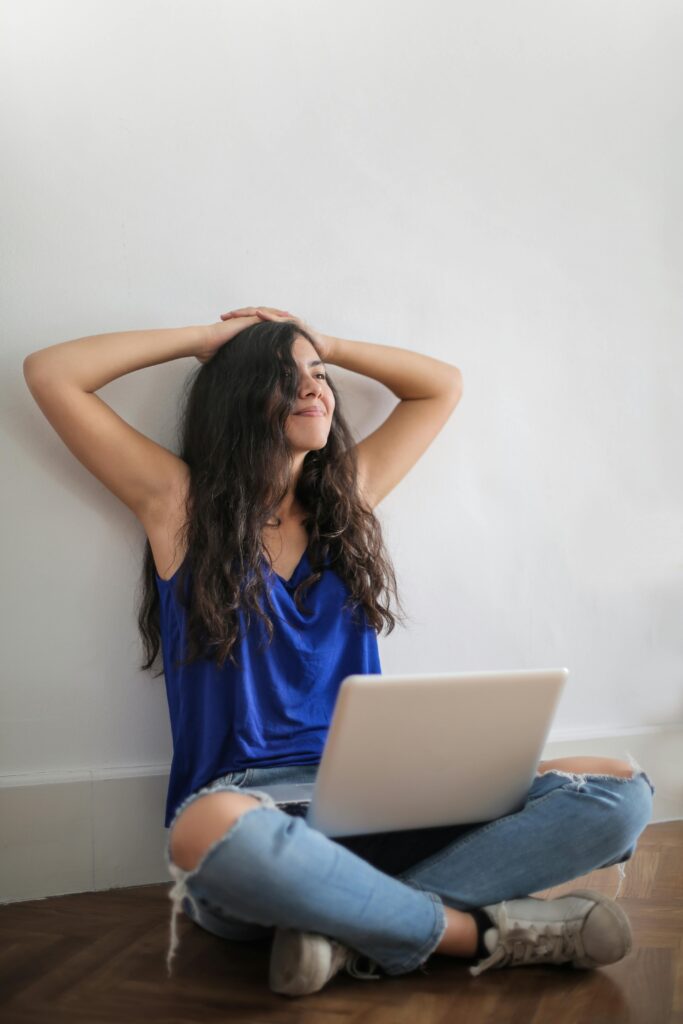 Young woman sitting indoors with laptop, smiling and relaxed. Comfortable casual style.